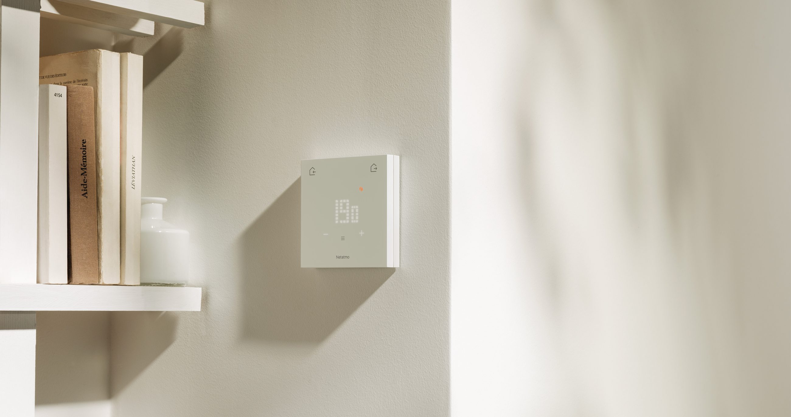 The ORIGINAL Thermostat on a light wall, next to a bookshelf
